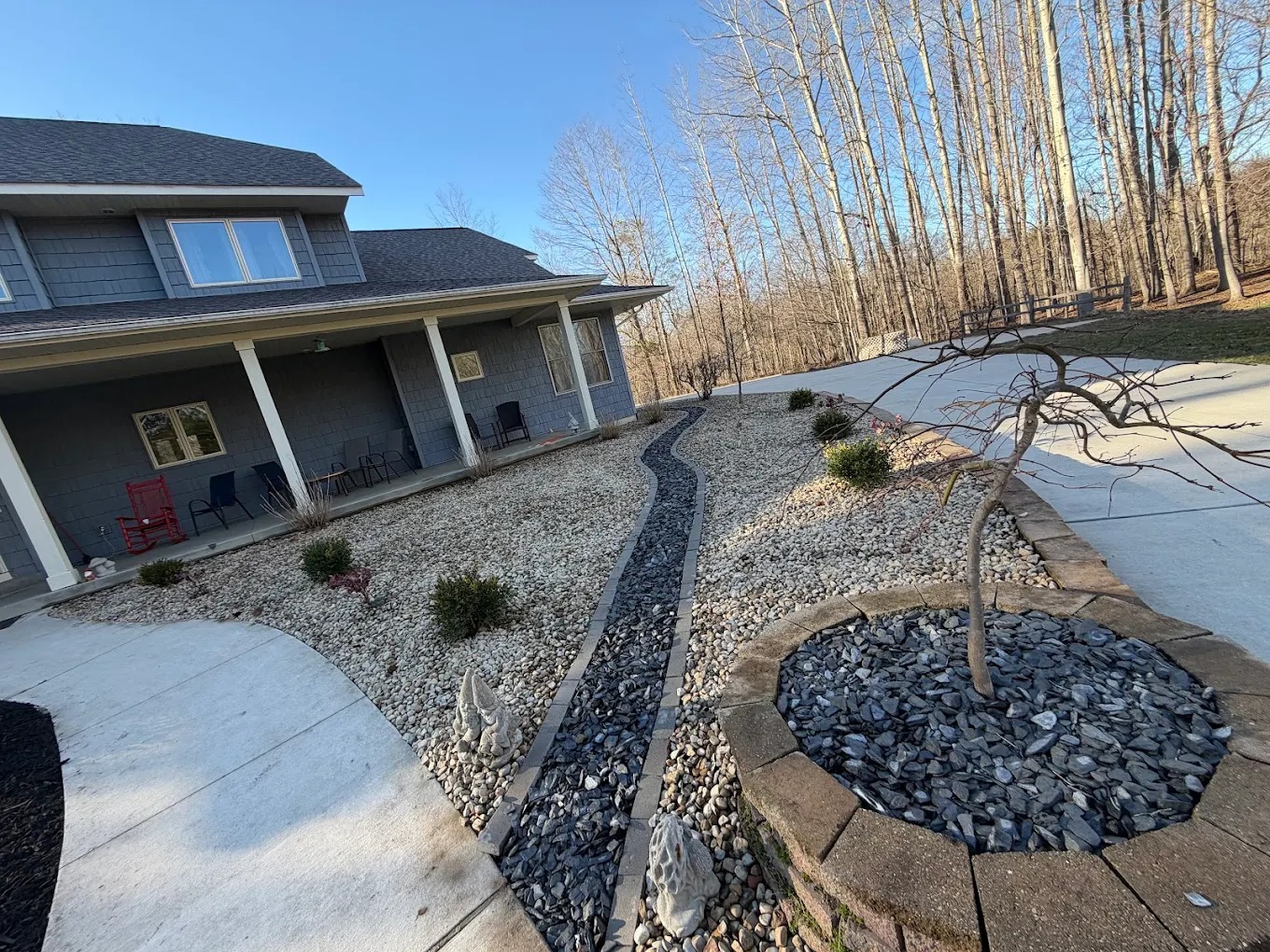Hardscaped front yard with river-rock beds, dry creek drainage, and stone-edged planter in Bangor, MI